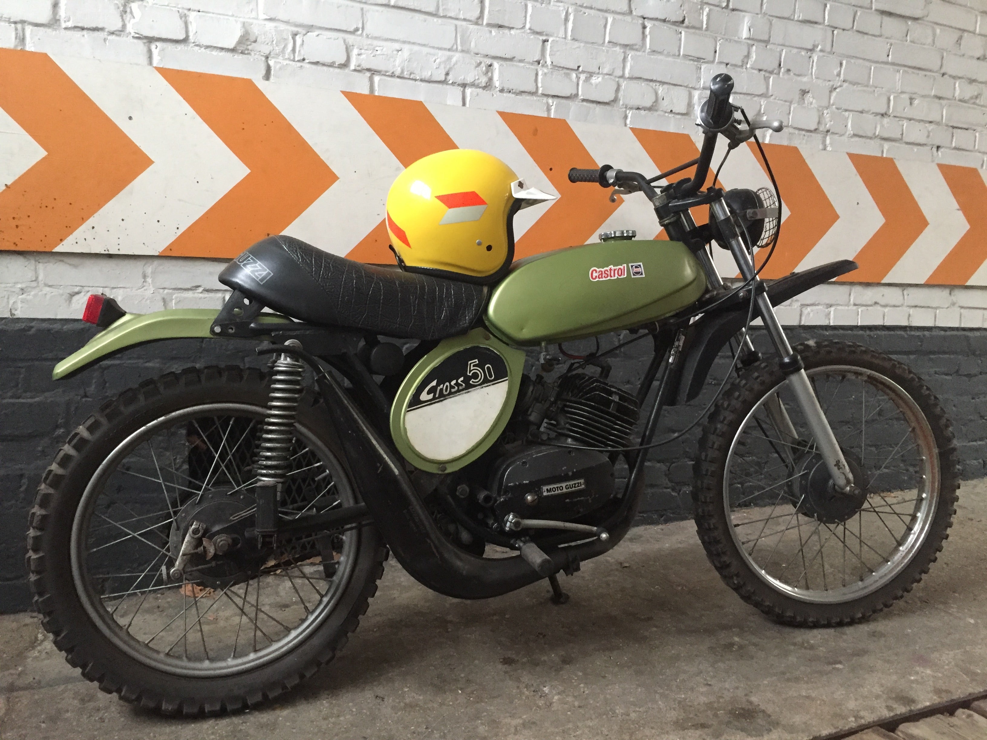 Moto Guzzi 50 Cross de 1970, moto vintage avec cadre et pneus colorés, vue de côté sur fond neutre.