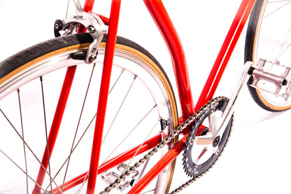 Vélo fixie Abici noir avec cadre léger, pneus épais et guidon droit, posé sur un fond urbain.